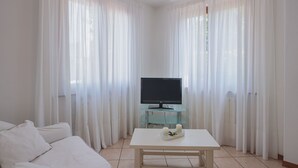 A living room with a white sofa, a glass coffee table with a TV and candles, and sheer white curtains. - Vacation home Rosa by Interhome (Lido di Camaiore)