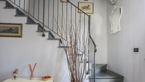 A staircase with a metal railing, a white console table with decorative items, and a vase with branches. - La Rondine (LUU280) by Interhome (Lucca)