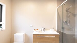Une salle de bain moderne comprenant des toilettes, un lavabo avec un meuble en bois, et une douche séparée par une paroi de verre.