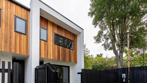 Une maison moderne à deux étages, dotée d’une façade en bois, d’une clôture noire et d’une pelouse bien entretenue.
