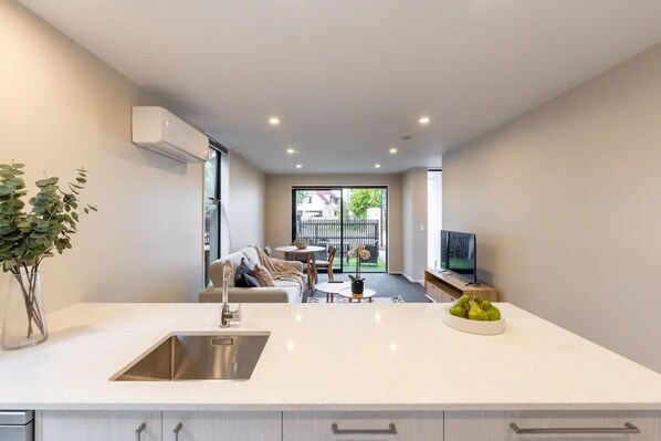 A modern kitchen with a built-in sink, a dining area with a table and chairs, and a living room with a sofa and a TV.