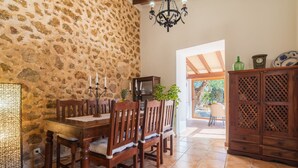 A dining area with a stone wall, wooden table and chairs, a chandelier, and a view of the outdoors. - Son Catlar by Interhome (Inca)