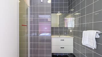 Une salle de bain moderne avec une douche à l’italienne en verre, un lavabo blanc avec un miroir au-dessus et une serviette accrochée au mur.