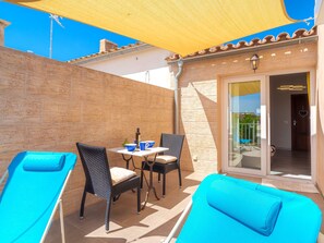 Une terrasse ensoleillée avec une table, des chaises et un fauteuil de jardin bleu.