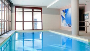 An indoor swimming pool with clear glass walls, a tiled floor, and a mural of a snowboarder on a mountain.