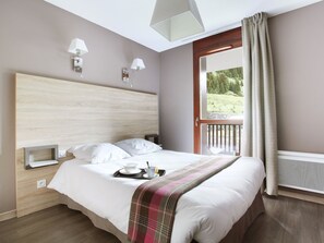 A modern bedroom with a large bed, bedside tables, a window with curtains, and a view of greenery outside.