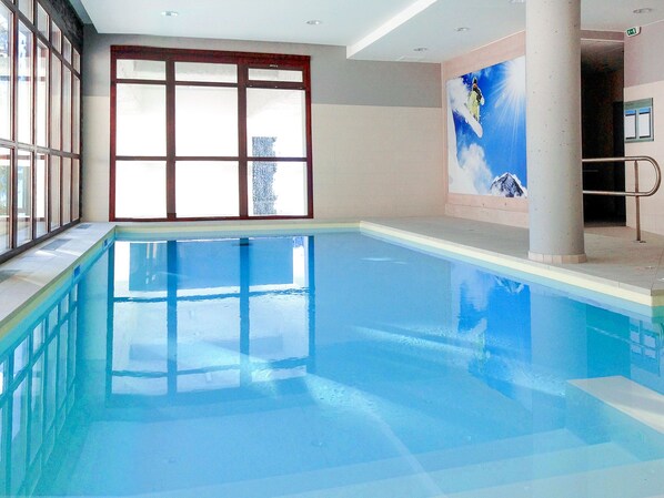 An indoor swimming pool with clear glass walls, a tiled floor, and a mural of a snowboarder on a mountain.