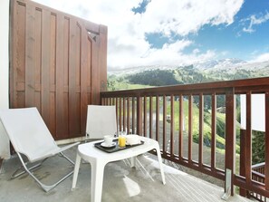 A balcony with two white chairs and a small table, overlooking a mountainous landscape.