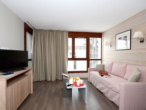 A modern living room with a flat-screen TV, a wooden coffee table with breakfast items, a pink sofa, and a large window with curtains.