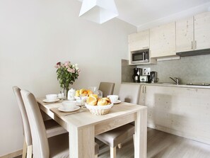 A dining area with a wooden table set for breakfast, including bread, fruit, and a vase of flowers.