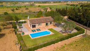 Vista aérea de uma villa com piscina, rodeada por vegetação e campos.