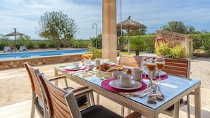 A dining table set outdoors with a pool view, surrounded by chairs and umbrellas. - Vacation home Marina by Interhome (Sa Rápita)