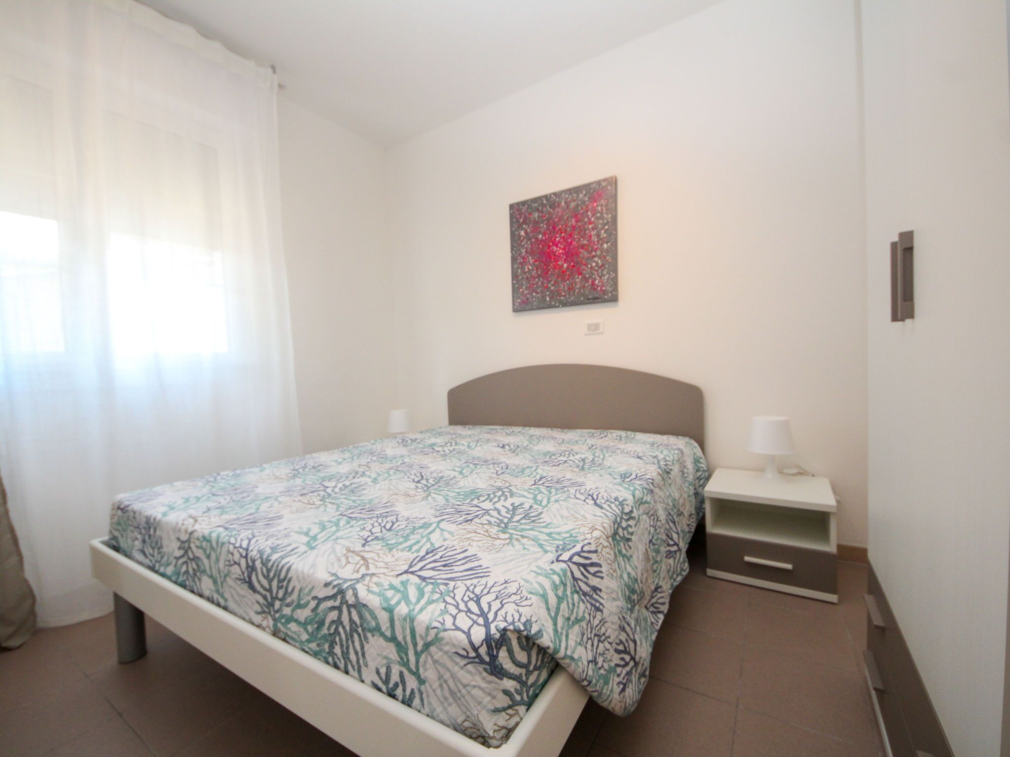 Une chambre à coucher comprenant un lit, une table de chevet, une lampe fixée au mur et un tableau.
