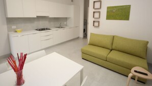 A modern kitchen with white cabinets, a dining table, and a green sofa in a living area. - Marcello by Interhome (Rosolina Mare)