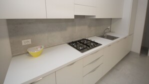A modern kitchen with white cabinets, a gas stove, a sink, and a yellow bowl on the countertop. - Marcello by Interhome (Rosolina Mare)