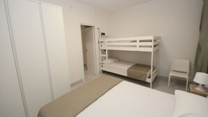 A bedroom with a bunk bed, a single bed, a wardrobe, a chair, and a bedside table with a lamp. - Marcello by Interhome (Rosolina Mare)