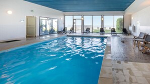 An indoor swimming pool with clear blue water, surrounded by lounge chairs and a view of the outdoors. - Odalys Domaine des Roches Jaunes by Interhome (Plougasnou)