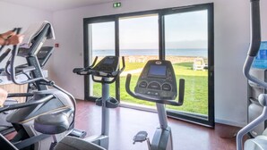 A gym with treadmills, a stationary bike, and a large window with a view of the beach. - Odalys Domaine des Roches Jaunes by Interhome (Plougasnou)