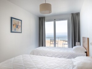 A hotel room with two beds, a large window with a view of the beach, and a framed picture on the wall.