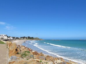 Vista costera con costa rocosa, una playa arenosa y edificios al fondo.