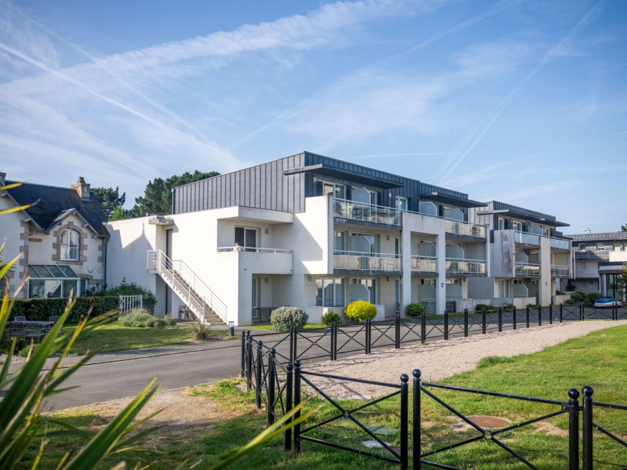 A modern multi-story building with a central staircase, a gated driveway, and a well-maintained lawn.