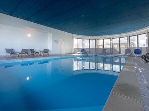 An indoor swimming pool with clear blue water, surrounded by lounge chairs and a curved ceiling.