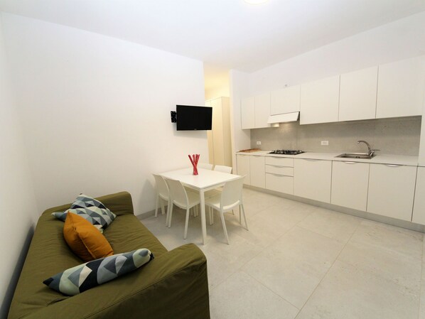 Un espacio habitable compacto con kitchenette, comedor y sofá con cojines.