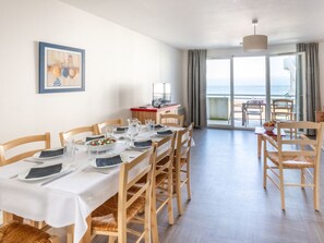 A dining area with a table set for six, wooden chairs, a television, and a view of the sea through large windows. - Odalys Domaine des Roches Jaunes by Interhome (Plougasnou)