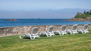 A row of white lounge chairs facing a stone wall with a view of the ocean and distant islands. - Odalys Domaine des Roches Jaunes by Interhome (Plougasnou)