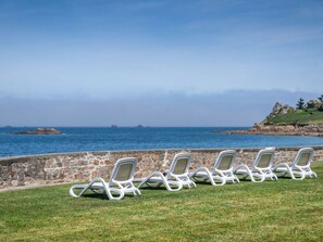 A row of white lounge chairs on a grassy area with a stone wall and ocean view. - Odalys Domaine des Roches Jaunes by Interhome (Plougasnou)