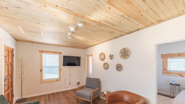 Een kamer met houten vloeren, een flatscreen televisie aan de muur, een grijze fauteuil, een bruine lederen stoel en een groene bank.
