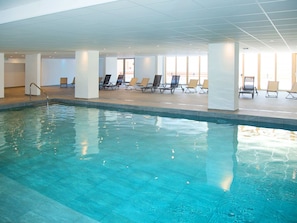 Une piscine intérieure à l’eau claire, entourée de chaises longues et dotée d’un sol carrelé.