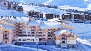 A snow-covered mountain resort with multi-story buildings, ski slopes, and a clear sky.