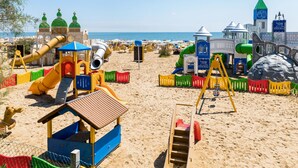 Ein Strandspielplatz mit verschiedenen Spielgeräten, darunter Rutschen und Klettergerüste, umgeben von Sand.