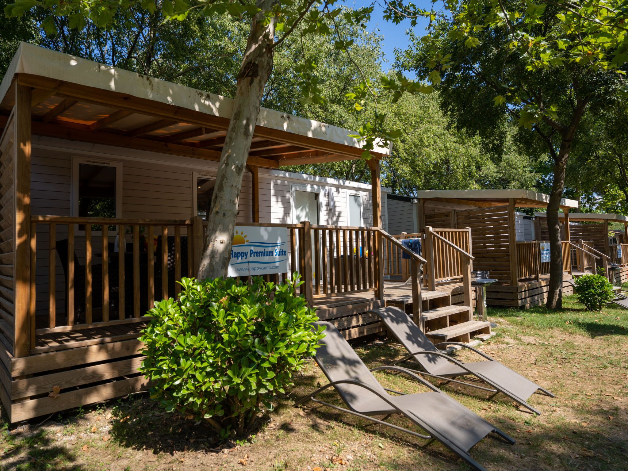 A campsite with wooden cabins, a sign for Happy Premium Suite, and a small garden area.