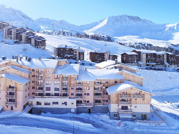 A snow-covered mountain resort with multi-story buildings, ski slopes, and a clear sky.