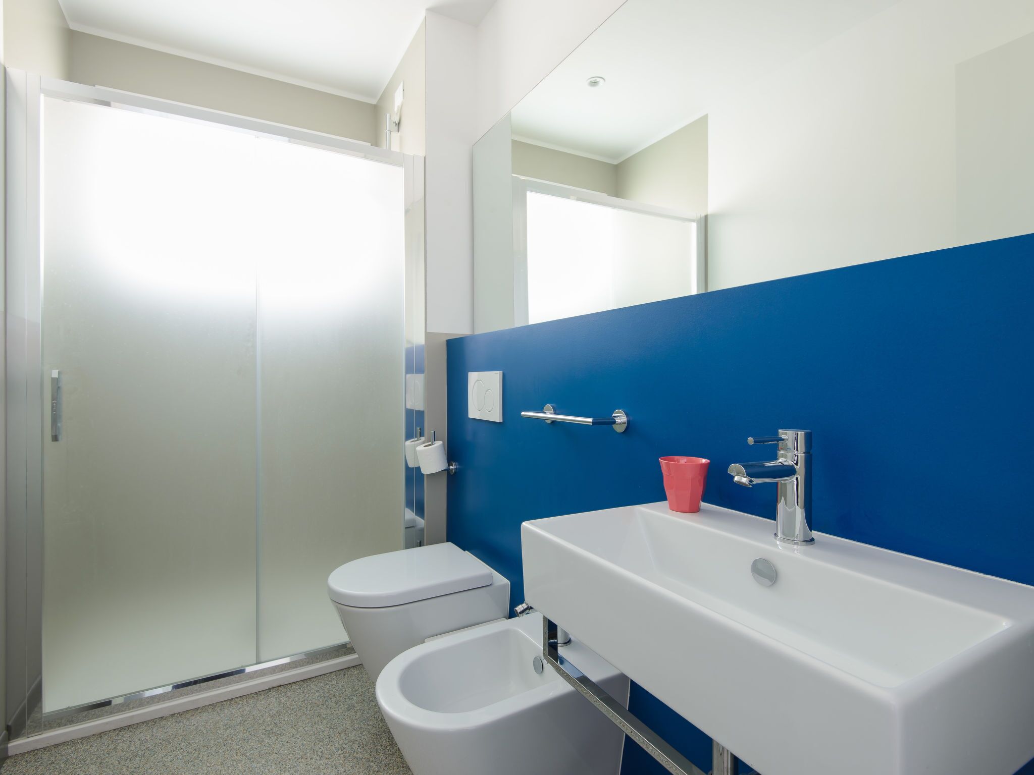 A modern bathroom with a white toilet, a bidet, and a sink with a red cup.