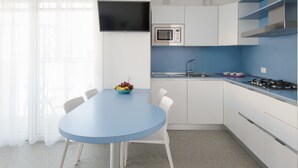 A modern kitchen with white cabinets, a blue countertop, a microwave, a gas stove, and a bowl of fruit on a table.