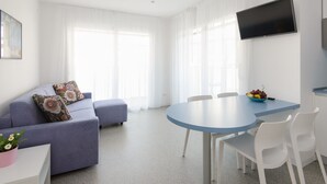 A modern living room with a sofa, a dining table with chairs, and a flat-screen TV mounted on the wall.