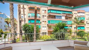 Un balcón con mobiliario de mimbre, vista a edificios de varios pisos y palmeras.
