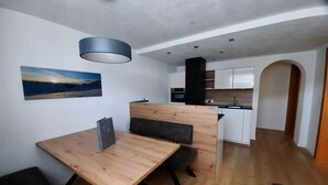 Una cuina moderna amb armaris blancs, una campana extractora negra i una zona menjador de fusta amb una banca.