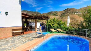 A swimming pool with a stone-tiled deck, a pergola, and a view of hills in the background.