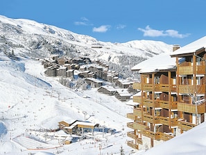 Un centro turístico en la montaña cubierto de nieve, con edificios de madera, pistas de esquí y un telesilla.