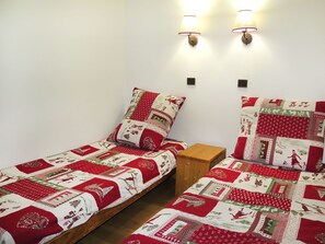Ein Doppelzimmer mit zwei Einzelbetten, jedes mit einer rot-weißen Bettdecke. Zwei Wandleselampen und ein kleiner Nachttisch aus Holz befinden sich zwischen den Betten.