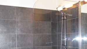 Un baño moderno con ducha envuelta en vidrio, un lavamanos blanco y paredes revestidas de baldosas oscuras.