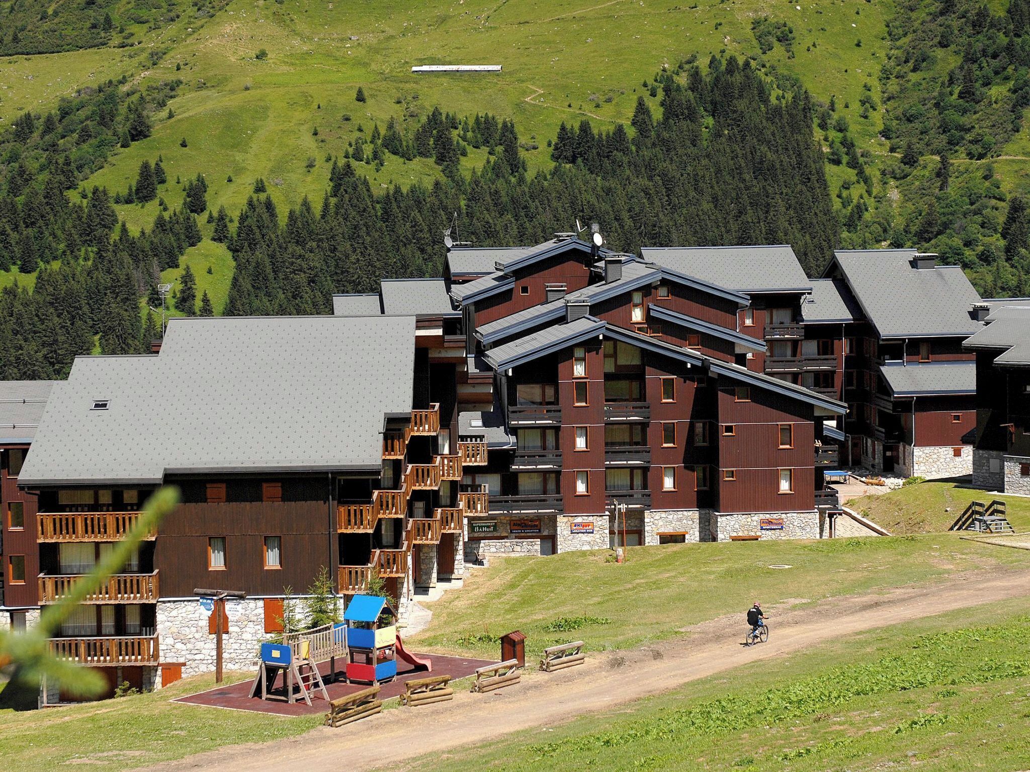 A multi-story hotel with a ski lift, surrounded by green hills and trees.