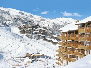 Un centro turístico en la montaña cubierto de nieve, con edificios de madera, pistas de esquí y un telesilla.