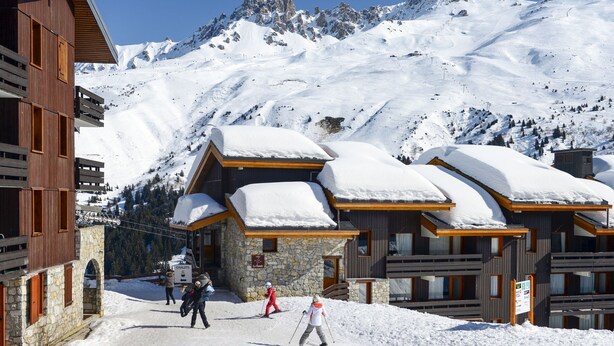 Une station de montagne enneigée, avec des bâtiments en bois et des murs en pierre.