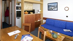 Un espace de vie compact comprenant un coin cuisine, un coin repas et un coin salon avec un canapé bleu.