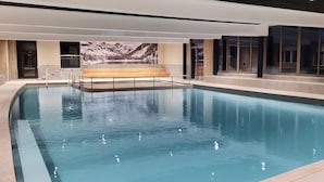 A large indoor swimming pool with clear blue water, a wooden bench, and a mountain landscape mural on the wall. - Résidence Odalys Collection L'Eclose by Interhome (L'Alpe d'Huez)
